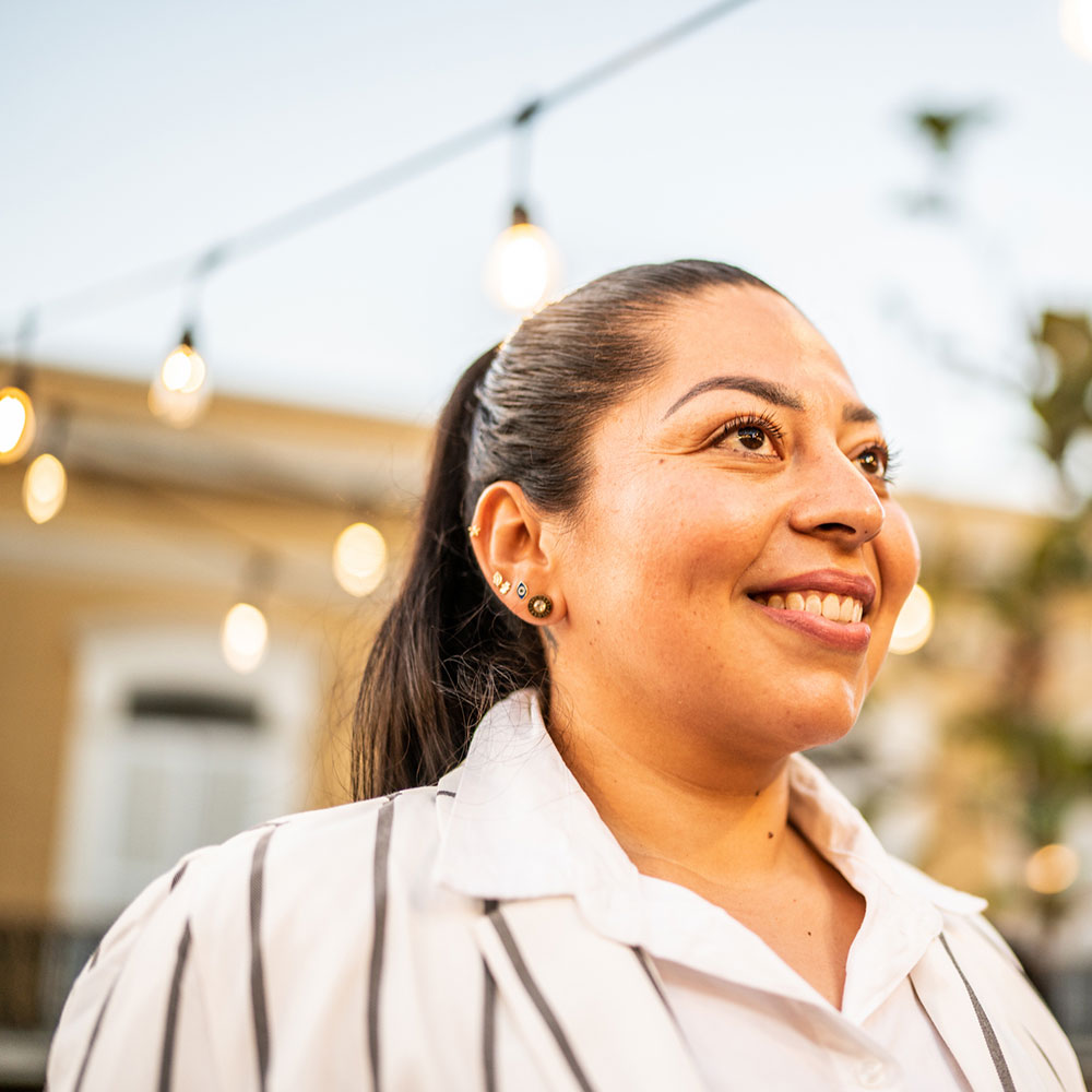 a woman in a patio garden smiles, she is framed by lights