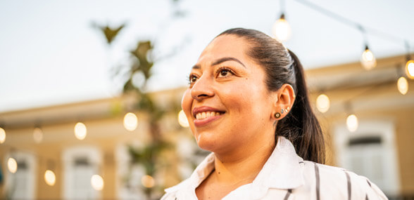 a woman in a patio garden smiles, she is framed by lights