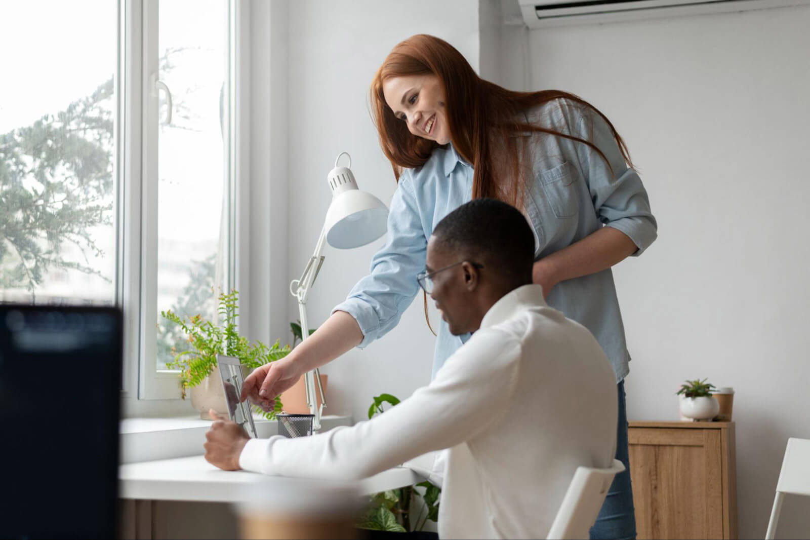 A woman smiles while assisting a man at a desk, illustrating supportive interactions that can reduce stress.