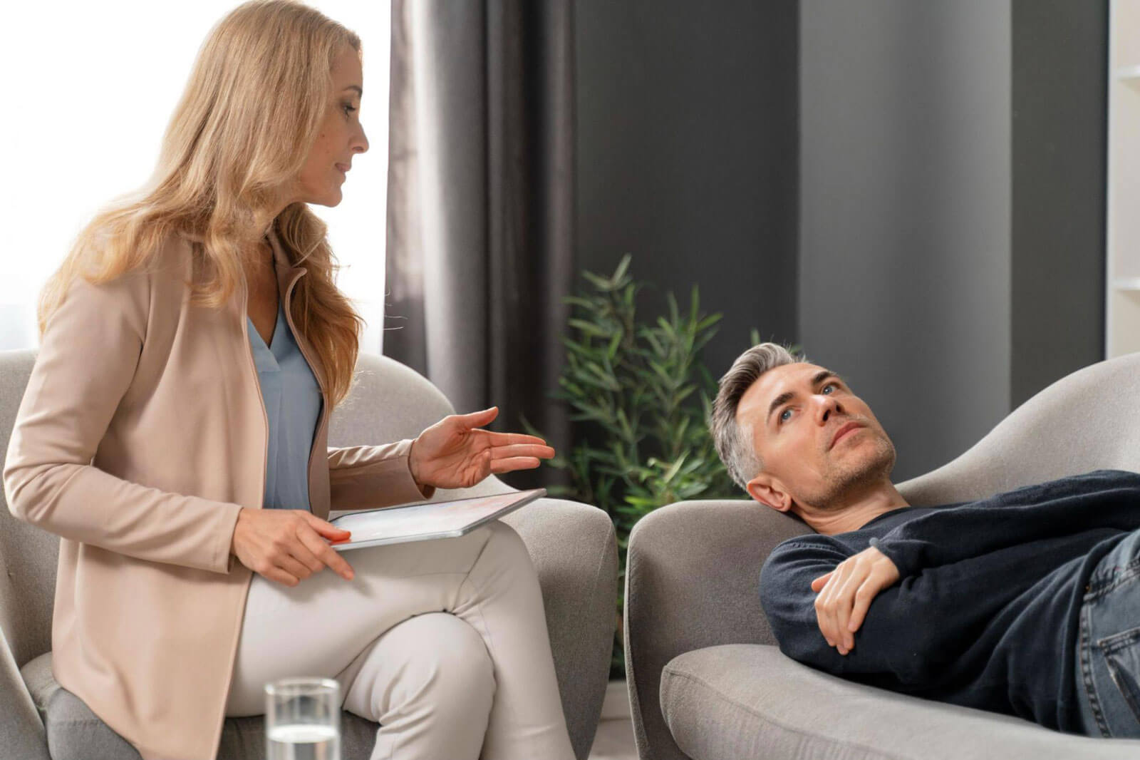 A therapist speaking with a man lying on a chair, illustrating a calm, nonjudgmental setting focused on understanding challenges and supporting continued progress.