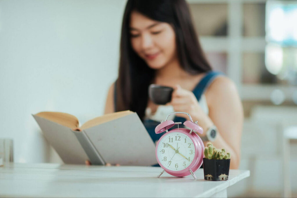 A woman reading a book with a cup of coffee beside a clock, illustrating how healthy routines, personal accountability, mindfulness, and daily structure support long-term addiction recovery.