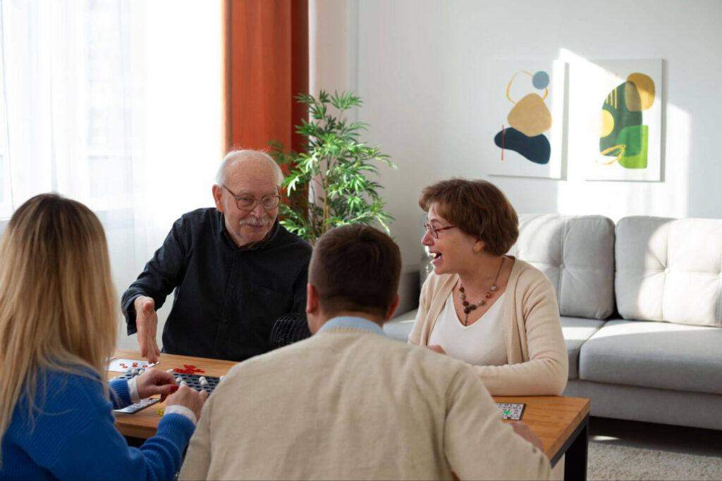 Four adults sitting around a table in a bright living room, laughing and playing a board game together.