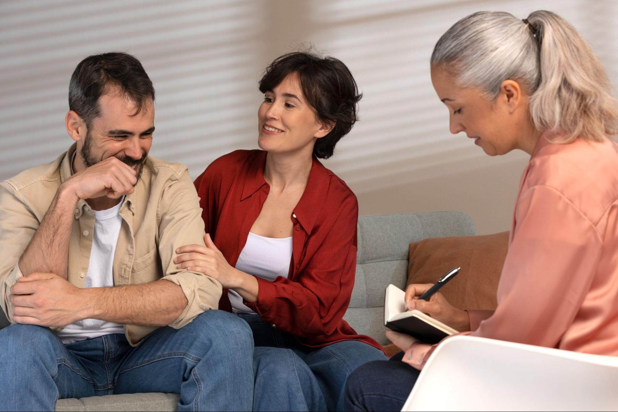 Man laughing while a woman comforts his arm and a counselor takes notes beside them.
