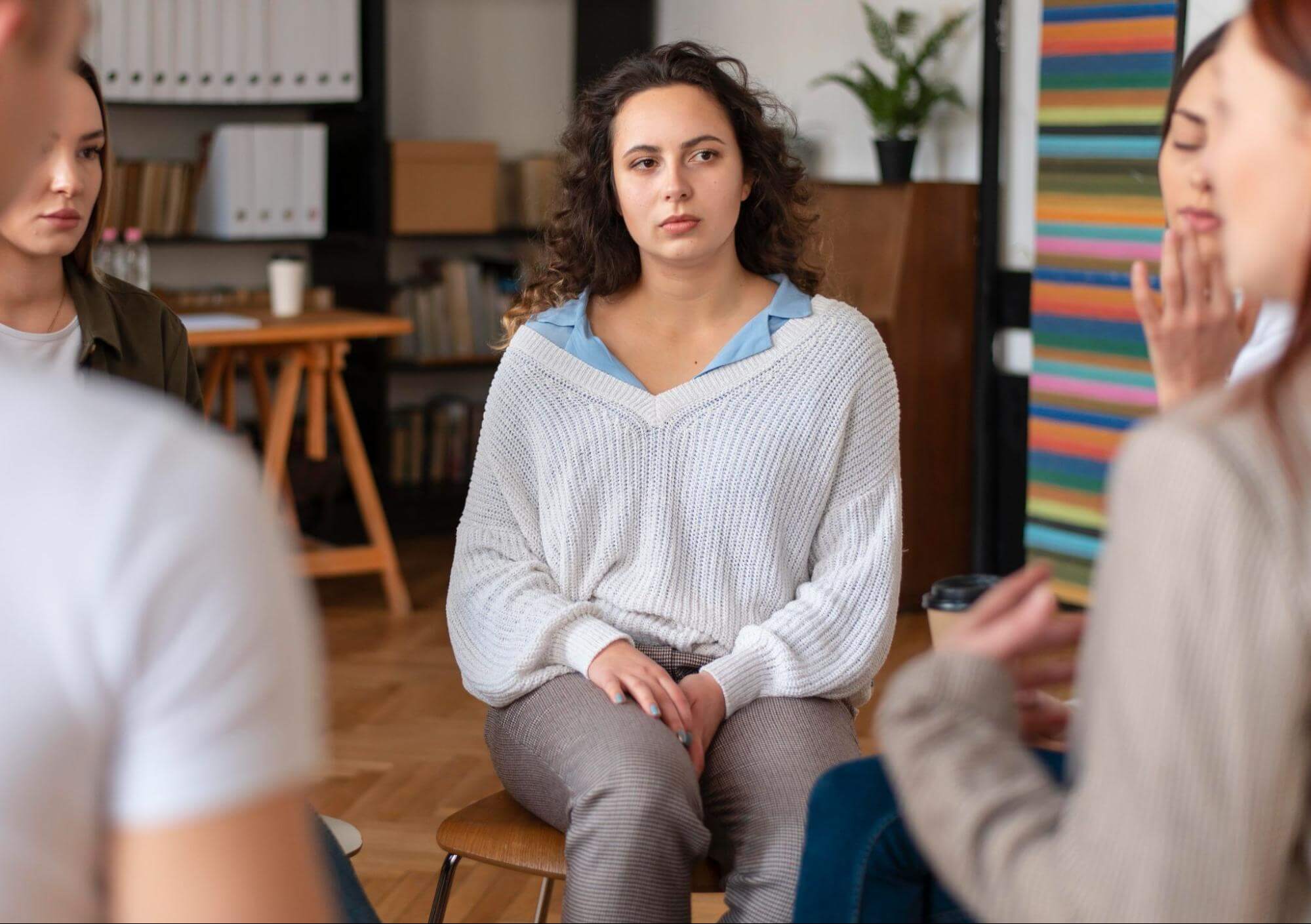 Serious young woman sitting in a chair surrounded by others during a group session.